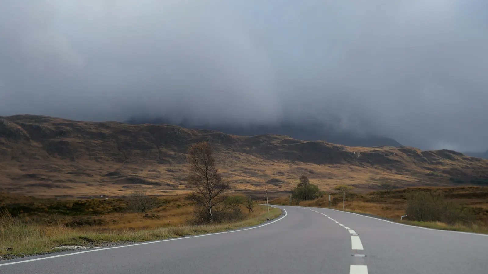 An empty road curving through brown moorland under low grey cloud